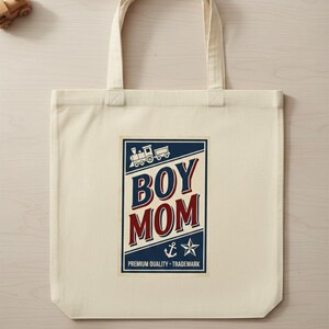Puede incluir: Bolso tote de color crema con un gr&aacute;fico rectangular. El gr&aacute;fico presenta las palabras "BOY MOM" en rojo y azul, una ilustraci&oacute;n de tren, un ancla y una estrella. Tambi&eacute;n se incluye el texto "PREMIUM QUALITY - TRADEMARK".