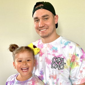 May include: A father and daughter wearing matching tie-dye shirts. The father's shirt says "Girl Dad" and the daughter's shirt says "Daddy's Girl".