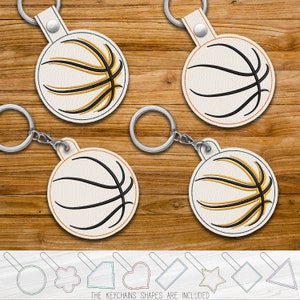 May include: Four white leather keychains with a basketball design. The basketballs have black outlines and yellow stitching. The keychains are on a wooden background. The text "THE KEYCHAINS SHAPES ARE INCLUDED" is at the bottom of the image.