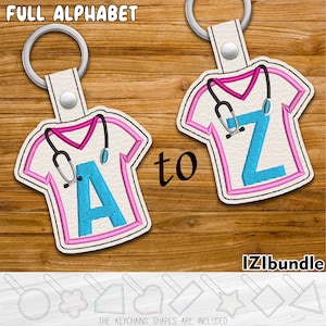 May include: A set of 26 alphabet letter keychains, each featuring a blue letter on a pink shirt with a stethoscope. The keychains are made of white leather and come with a variety of keychain shapes, including a circle, flower, rectangle, heart, star, and triangle.