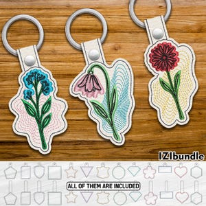 Puede incluir: Tres llaveros bordados con flores y aros plateados. Las flores son en tonos de azul, rosa y rojo, con tallos y hojas verdes. Los llaveros están sobre una superficie de madera. El texto "IZIbundle" y "ALL OF THEM ARE INCLUDED" son visibles.