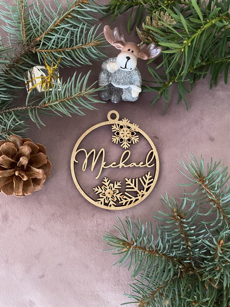 Pu&ograve; includere: Un ornamento natalizio in legno con il nome "Michael" scritto in corsivo. L'ornamento &egrave; decorato con fiocchi di neve e ha uno spago marrone per appenderlo.