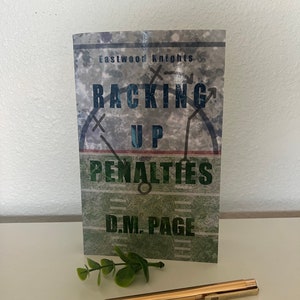 May include: A book cover with a green and brown camouflage pattern. The title is "Racking Up Penalties" with the words "Eastwood Knights" at the top and "D.M. Page" at the bottom.