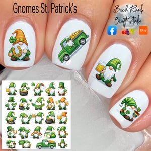 Könnte beinhalten: Nagelkunst mit St. Patrick's Day Zwergen-Designs. Die Designs zeigen Zwerge mit Bier, Goldtöpfen und einem grünen Lastwagen voller Goldmünzen. Die Nägel sind weiß lackiert und mit den Zwergen-Designs versehen. Der Text "Gnomes St. Patrick's" steht oben.