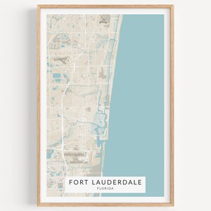 May include: A beige and blue map print of Fort Lauderdale, Florida. The map shows the city's streets, waterways, and coastline. The city name and state are printed at the bottom of the map.