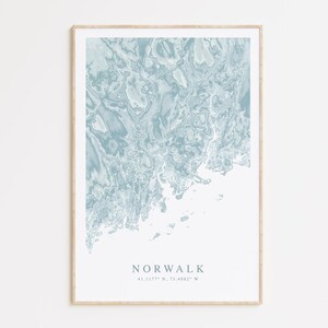 May include: A blue and white abstract map print of Norwalk, Connecticut. The print is framed in a light wood frame. The text "NORWALK 41.1277° N, 73.4082° W" is printed below the map.