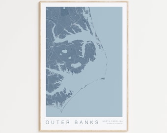 May include: A blue and white map print of the Outer Banks, North Carolina. The print is framed in a light wood frame.