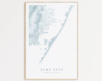 May include: A framed print of a blue and white map of Surf City, North Carolina. The map shows the coastline and surrounding area. The text "Surf City" and the coordinates "39.6621° N, 74.1651° W" are printed below the map.