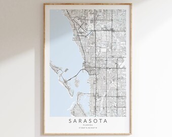 May include: A black and white map of Sarasota, Florida, with a light blue background. The map shows the city's streets and waterways. The text "SARASOTA" is printed in black at the bottom of the map, along with the coordinates "27.3365° N, 82.5339° W".