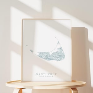 K&ouml;nnte beinhalten: Ein gerahmter Druck einer Karte der Insel Nantucket, Massachusetts. Die Karte ist in hellblau gehalten und von einem wei&szlig;en Rahmen umgeben. Der Text "NANTUCKET 41.2839&deg; N, 70.0807&deg; W" ist unter der Karte gedruckt.