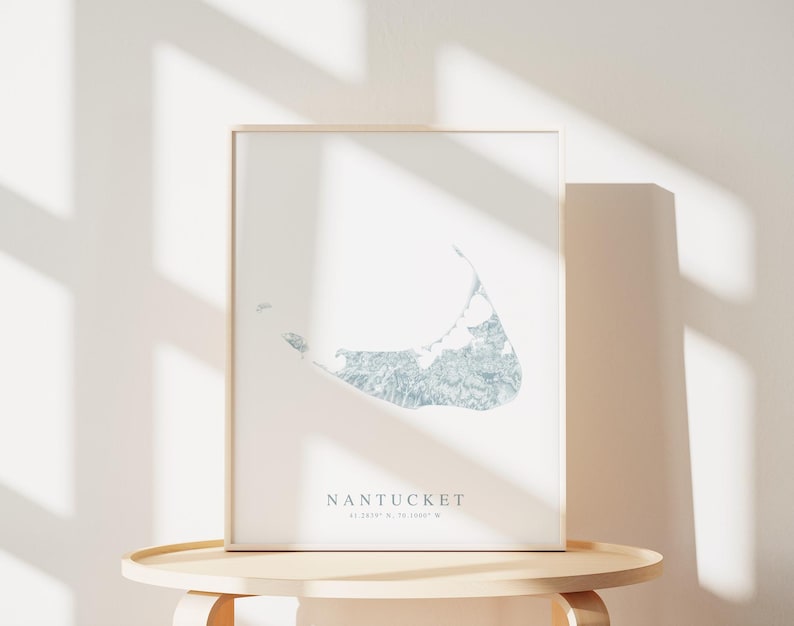 K&ouml;nnte beinhalten: Ein gerahmter Druck einer Karte der Insel Nantucket, Massachusetts. Die Karte ist in hellblau gehalten und von einem wei&szlig;en Rahmen umgeben. Der Text "NANTUCKET 41.2839&deg; N, 70.0807&deg; W" ist unter der Karte gedruckt.