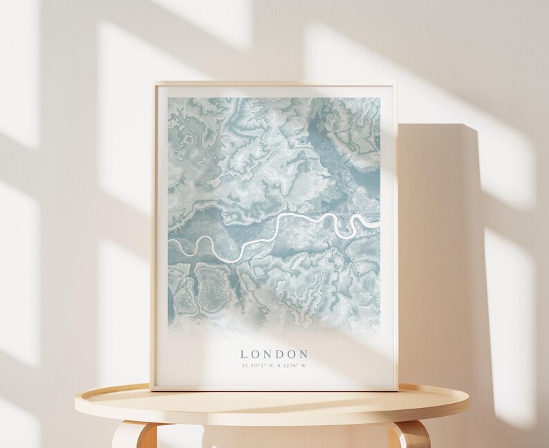 May include: A framed print of a map of London in a light blue color scheme. The map shows the Thames River winding through the city. The text "LONDON" is printed below the map, along with the coordinates "51.5072&deg; N, 0.1275&deg; W".