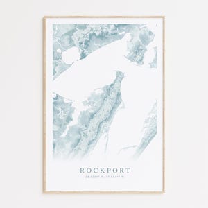 May include: A framed watercolor print of a coastal map in shades of blue and white. The map is titled "Rockport" with the coordinates "28.0204° N, 97.0544° W".