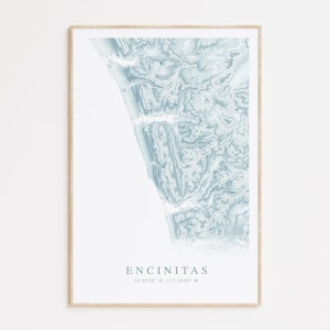 May include: A framed print of a topographic map of Encinitas, California. The map is in shades of blue and white, with the coastline highlighted in a darker blue. The text "Encinitas" and the coordinates "33.0170° N, 117.2920° W" are printed below the map.
