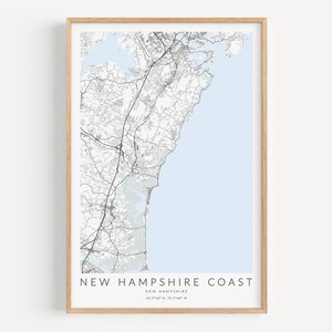 K&ouml;nnte beinhalten: Ein Schwarzwei&szlig;-Kartenabdruck der K&uuml;ste von New Hampshire mit hellblauem Hintergrund. Die Karte ist in einem hellen Holzrahmen gerahmt. Der Text "NEW HAMPSHIRE COAST" ist unter der Karte gedruckt, zusammen mit den Koordinaten "42.7164&deg; N, 70.7348&deg; W".