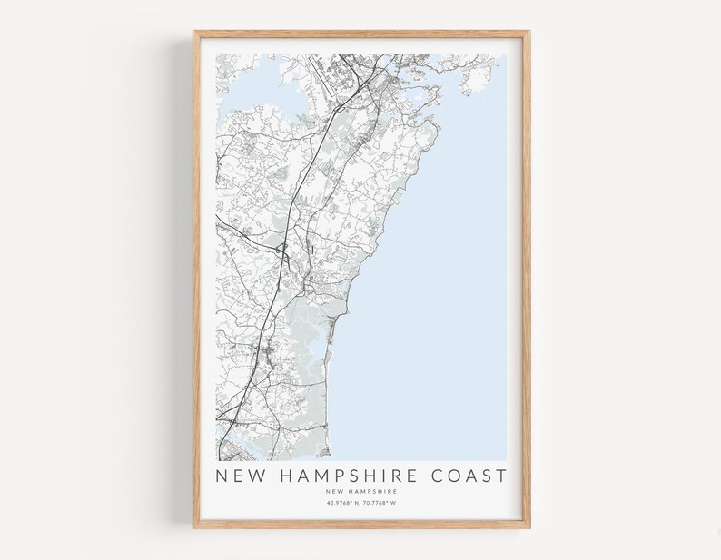 K&ouml;nnte beinhalten: Ein Schwarzwei&szlig;-Kartenabdruck der K&uuml;ste von New Hampshire mit hellblauem Hintergrund. Die Karte ist in einem hellen Holzrahmen gerahmt. Der Text "NEW HAMPSHIRE COAST" ist unter der Karte gedruckt, zusammen mit den Koordinaten "42.7164&deg; N, 70.7348&deg; W".