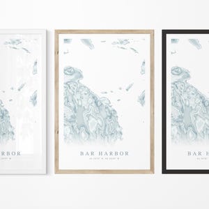 May include: Three framed prints of a map of Bar Harbor, Maine. The prints are in white, natural wood, and black frames. Each print features a blue and white topographic map of the area with the text "Bar Harbor" and coordinates.