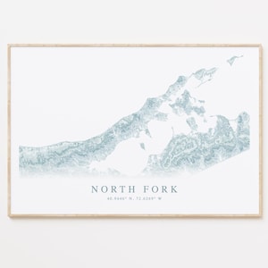 May include: A framed print featuring a topographical map of North Fork in shades of blue and white. The text "NORTH FORK" is centered below the map, along with the coordinates 40.9446° N, 72.6269° W. The print is in a light-colored wooden frame.