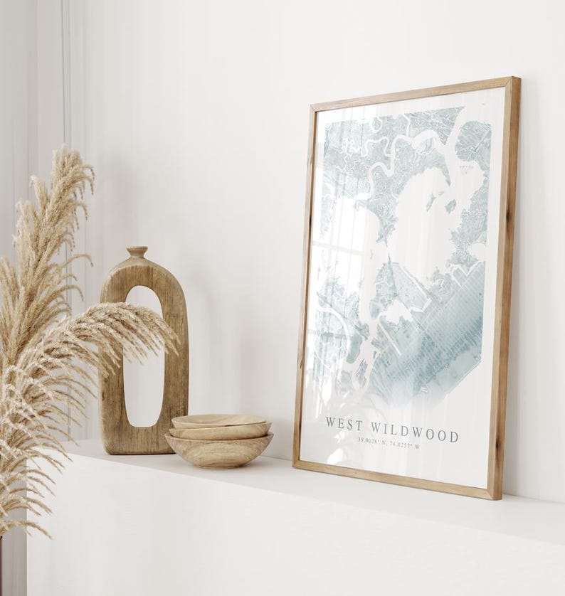 May include: A framed print with a light blue and white abstract design, labeled "WEST WILDWOOD". The print is in a light wood frame, displayed with wooden bowls, a decorative wooden sculpture, and dried pampas grass. The overall aesthetic is minimalist and natural.