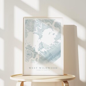 May include: A framed map print of West Wildwood, featuring a detailed blue and white topographical design. The print is displayed on a light-colored wooden table, with the text "WEST WILDWOOD" at the bottom. Coordinates are also included.