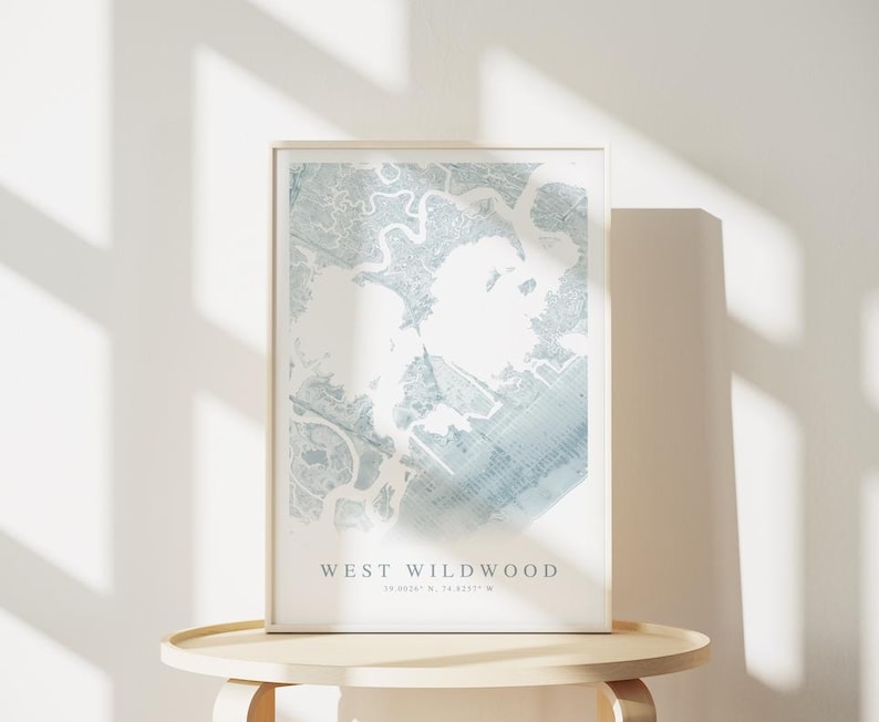 May include: A framed map print of West Wildwood, featuring a detailed blue and white topographical design. The print is displayed on a light-colored wooden table, with the text "WEST WILDWOOD" at the bottom. Coordinates are also included.
