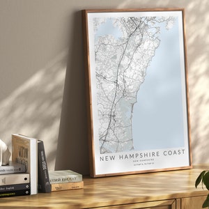 K&ouml;nnte beinhalten: Ein gerahmter Kartenabdruck der K&uuml;ste von New Hampshire mit hellblauem Hintergrund und schwarzen Linien, die die Stra&szlig;en und die K&uuml;ste zeigen. Der Text "NEW HAMPSHIRE COAST" ist in Schwarz am unteren Rand der Karte gedruckt.