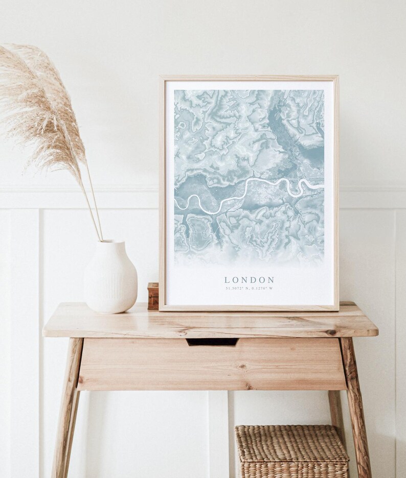 May include: A framed print of a blue and white map of London, England. The map shows the city's streets and waterways. The text "LONDON" and the coordinates "51.5074&deg; N, 0.1278&deg; W" are printed below the map.