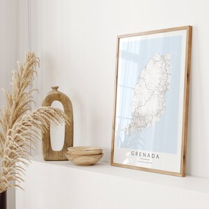 May include: A framed map of Grenada, a Caribbean island, with a light blue background and black lines representing roads and rivers. The frame is made of natural wood and the map is titled "Grenada, Caribbean, 12.11&deg;N 61.68&deg;W".