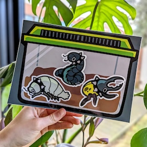 Op de afbeelding: Een sticker van een doorzichtige plastic container met drie cartoonbeestjes erin. De beestjes zijn een zwart-blauwe worm, een wit-grijze pissebed en een geel-zwarte kever.