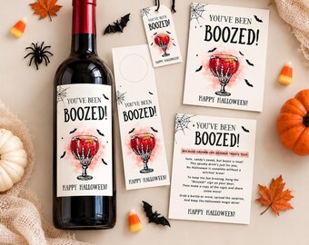 Könnte beinhalten: Eine Weinflasche mit Halloween-Etikett, das eine Skeletthand mit einem roten Getränk zeigt, dazu ein Flaschenanhänger, ein Geschenkanhänger und zwei Anleitungskarten. Alle Artikel tragen den Text YOU'VE BEEN BOOZED! und HAPPY HALLOWEEN mit Spinnennetzen.