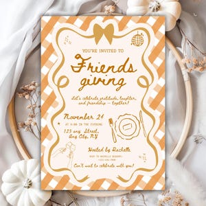 Può includere: Un invito per una festa del Ringraziamento tra amici. Il design presenta un motivo a quadretti vichy arancione chiaro e bianco con nastri decorativi e un fiocco. Il testo recita "Friendsgiving" e include i dettagli dell'evento come data, ora e luogo.