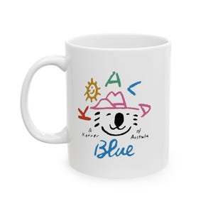 Könnte beinhalten: Weiße Keramiktasse mit einer bunten Illustration eines Koalas mit Hut und dem Text "A Korner of Australia Blue".