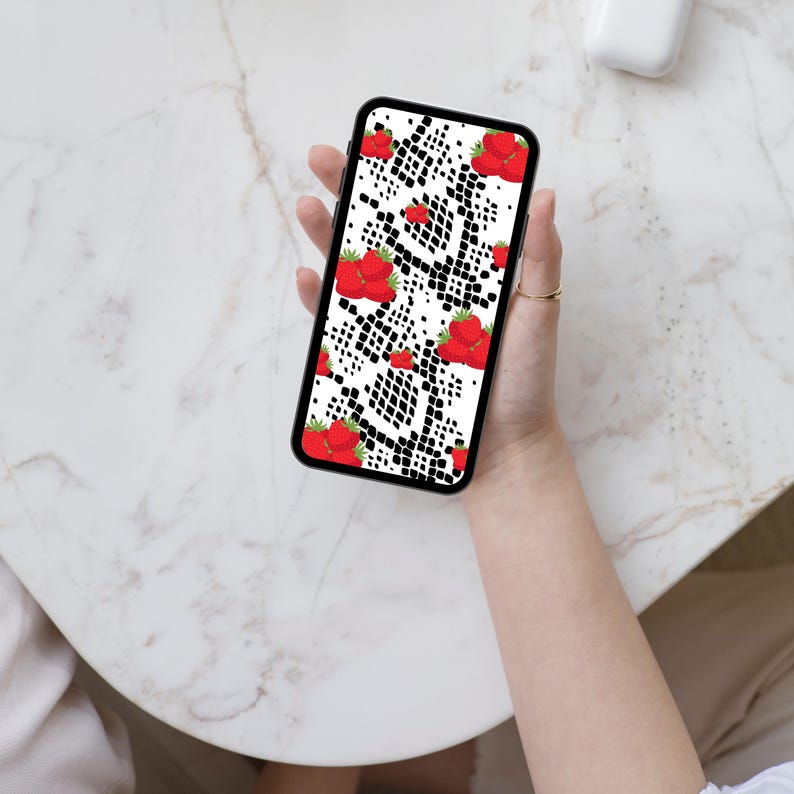 May include: A smartphone featuring a protective case with a white background, a black snakeskin pattern, and a repeating print of bright red strawberries with green leaves scattered across the surface of the device screen and case.