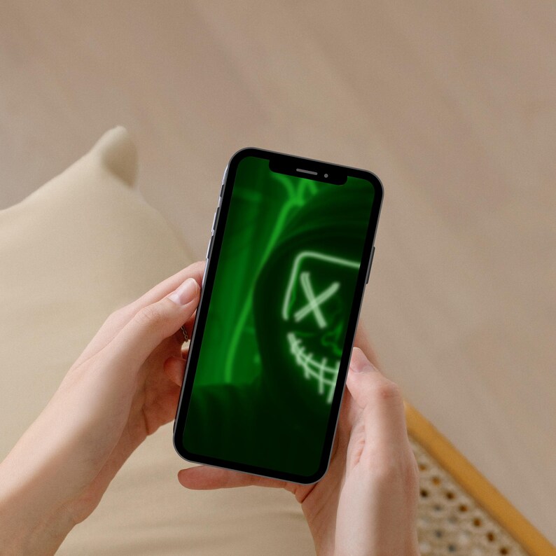 May include: A smartphone displaying a vibrant green digital wallpaper featuring a hooded figure wearing a mask with an X-shaped eye design and a stitched mouth. The screen shows a high-contrast graphic illustration with neon green glowing lines.