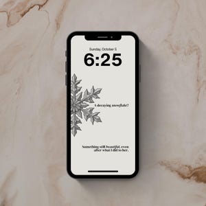 以下が含まれることがあります： 黒いスマートフォンには、6時25分、日付、グレースケールの雪の結晶のイラストが表示されたロック画面が表示されます。「A decaying snowflake?」と「Something still beautiful, even after what I did to her.」というテキストが表示されます。