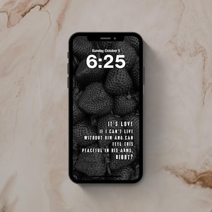 May include: A black smartphone displaying a lock screen with a black and white strawberry background. The screen shows the time 6:25, the date Sunday, October 5, and the text: IT'S LOVE IF I CAN'T LIVE WITHOUT HIM AND CAN FEEL THIS PEACEFUL IN HIS ARMS, RIGHT?