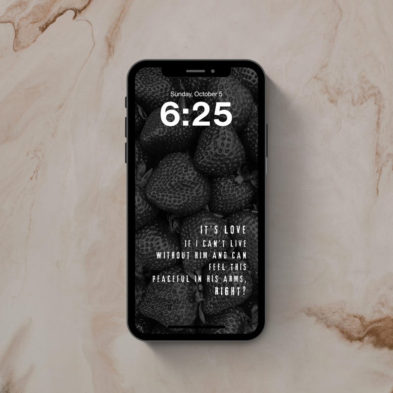 May include: A black smartphone displaying a lock screen with a black and white strawberry background. The screen shows the time 6:25, the date Sunday, October 5, and the text: IT'S LOVE IF I CAN'T LIVE WITHOUT HIM AND CAN FEEL THIS PEACEFUL IN HIS ARMS, RIGHT?