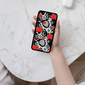 May include: A smartphone featuring a black screen with a repeating pattern of red strawberries and white snake-like scales. The device has a black frame and is held in a vertical orientation, displaying a vibrant, high-contrast graphic design.