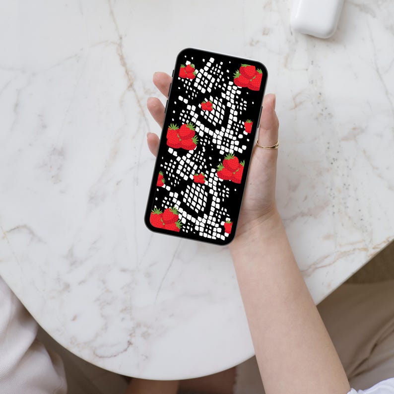 May include: A smartphone featuring a black screen with a repeating pattern of red strawberries and white snake-like scales. The device has a black frame and is held in a vertical orientation, displaying a vibrant, high-contrast graphic design.