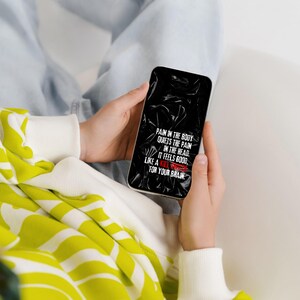 以下が含まれることがあります： 黒い背景に白い文字が表示されたスマートフォン。「PAIN IN THE BODY QUIETS THE PAIN IN THE HEAD. IT FEELS GOOD, LIKE A KILL SWITCH FOR YOUR BRAIN.」と書かれています。スマートフォンは両手で持たれています。