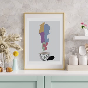 May include: A framed print of a stylised map of Lebanon in the shape of a coffee cup. The map is divided into different coloured regions. The cup is white with a black and white design and a green cedar tree in the centre.