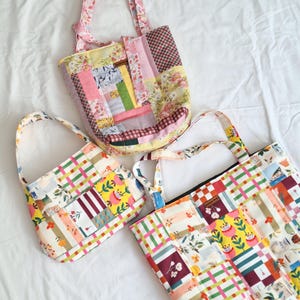 May include: Three quilted tote bags made from various fabric patches featuring floral, checkered, and striped patterns in shades of yellow, pink, green, and red. Each bag has two fabric handles and a rectangular or rounded base structure.