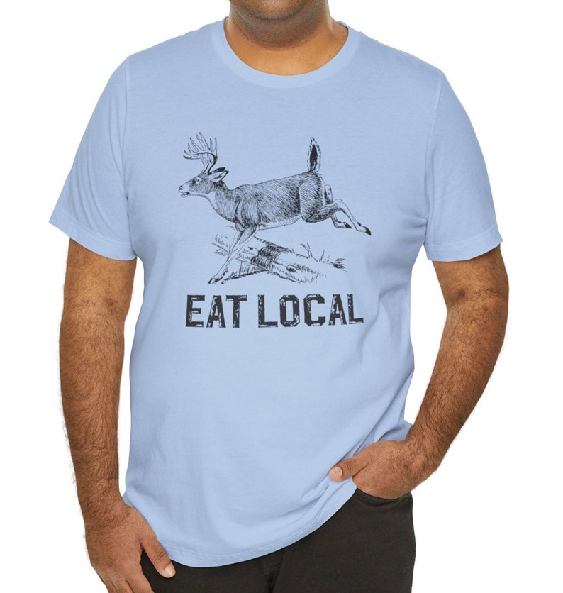 May include: Light blue t-shirt with a black and white illustration of a deer jumping over a log. The text "EAT LOCAL" is printed below the deer.