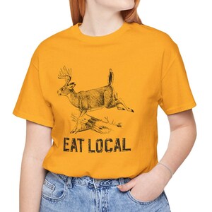 May include: A yellow t-shirt with a black and white illustration of a deer running. The text "EAT LOCAL" is printed below the deer.
