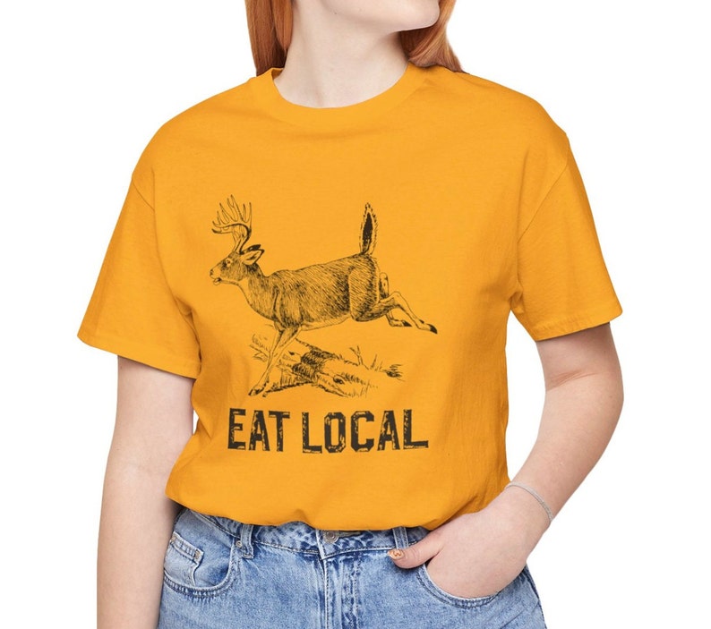 May include: A yellow t-shirt with a black and white illustration of a deer running. The text "EAT LOCAL" is printed below the deer.
