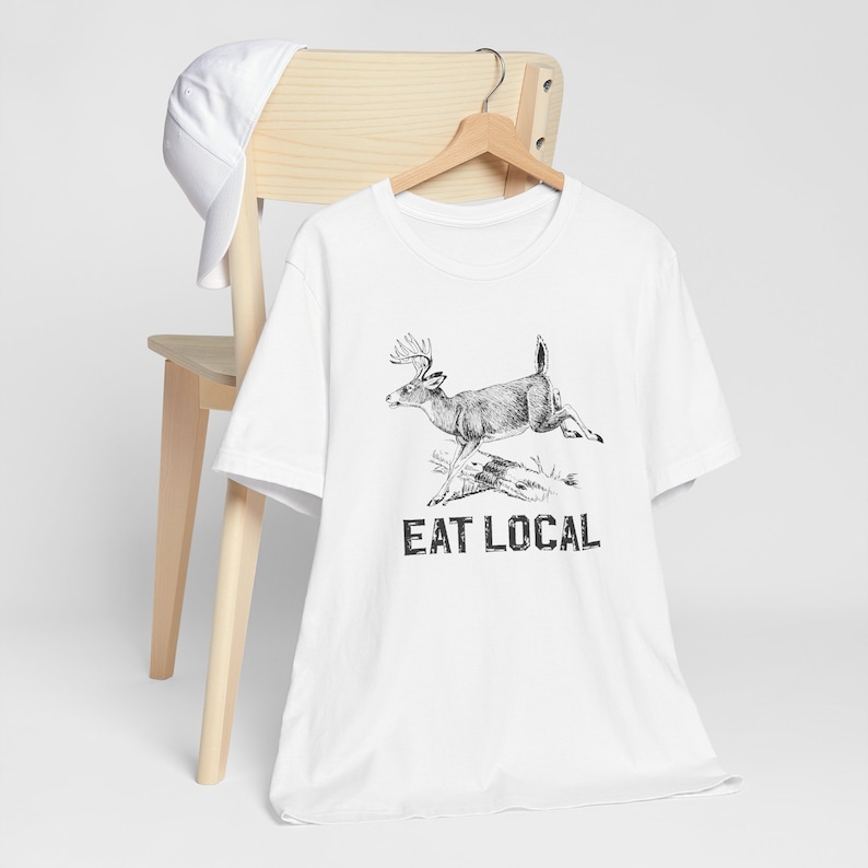 May include: White t-shirt with a black and white illustration of a deer jumping and the text "EAT LOCAL" printed on the front.