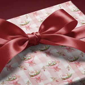 May include: A rectangular gift box wrapped in light pink and white gingham patterned paper featuring small illustrations of Santa Claus and holiday treats, tied with a wide, smooth, dark red satin ribbon bow across the top surface.