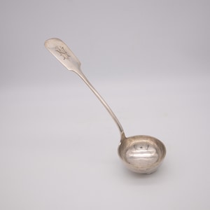 Può includere: Un mestolo d'argento con un manico lungo e una ciotola rotonda. Il manico è inciso con un monogramma.