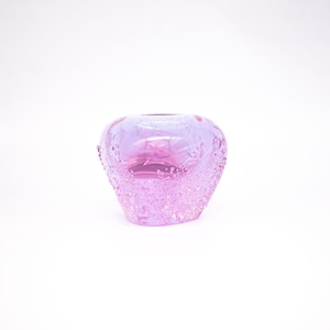 Puede incluir: Un pequeño jarrón redondo de cristal rosa con una superficie texturizada con forma de burbujas. El jarrón tiene una abertura ancha y una base ligeramente ensanchada. El color es un rosa suave y translúcido, y el diseño general es simple y elegante.