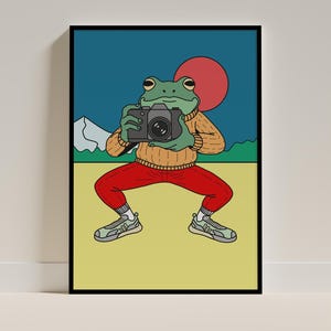Può includere: Una stampa artistica incorniciata con un cartone animato di una rana che tiene una macchina fotografica. La rana indossa un maglione beige, pantaloni rossi e scarpe da ginnastica. Lo sfondo include un sole rosso, montagne e un cielo blu. Lo stile artistico è moderno e stravagante.